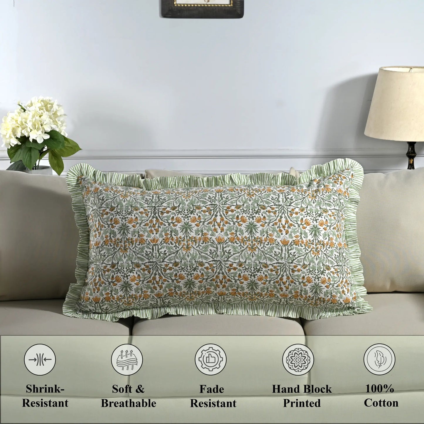 Cotton block print pillow cover placed on a bed with lamp and flowers in background.