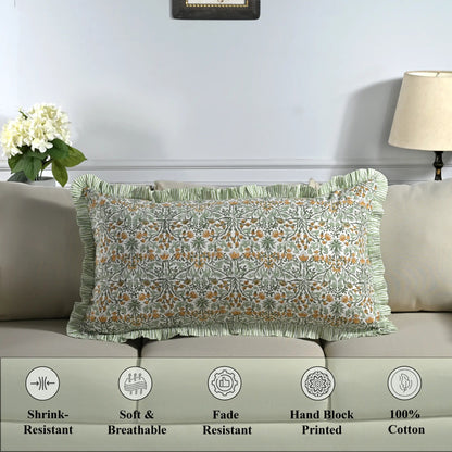 Cotton block print pillow cover placed on a bed with lamp and flowers in background.