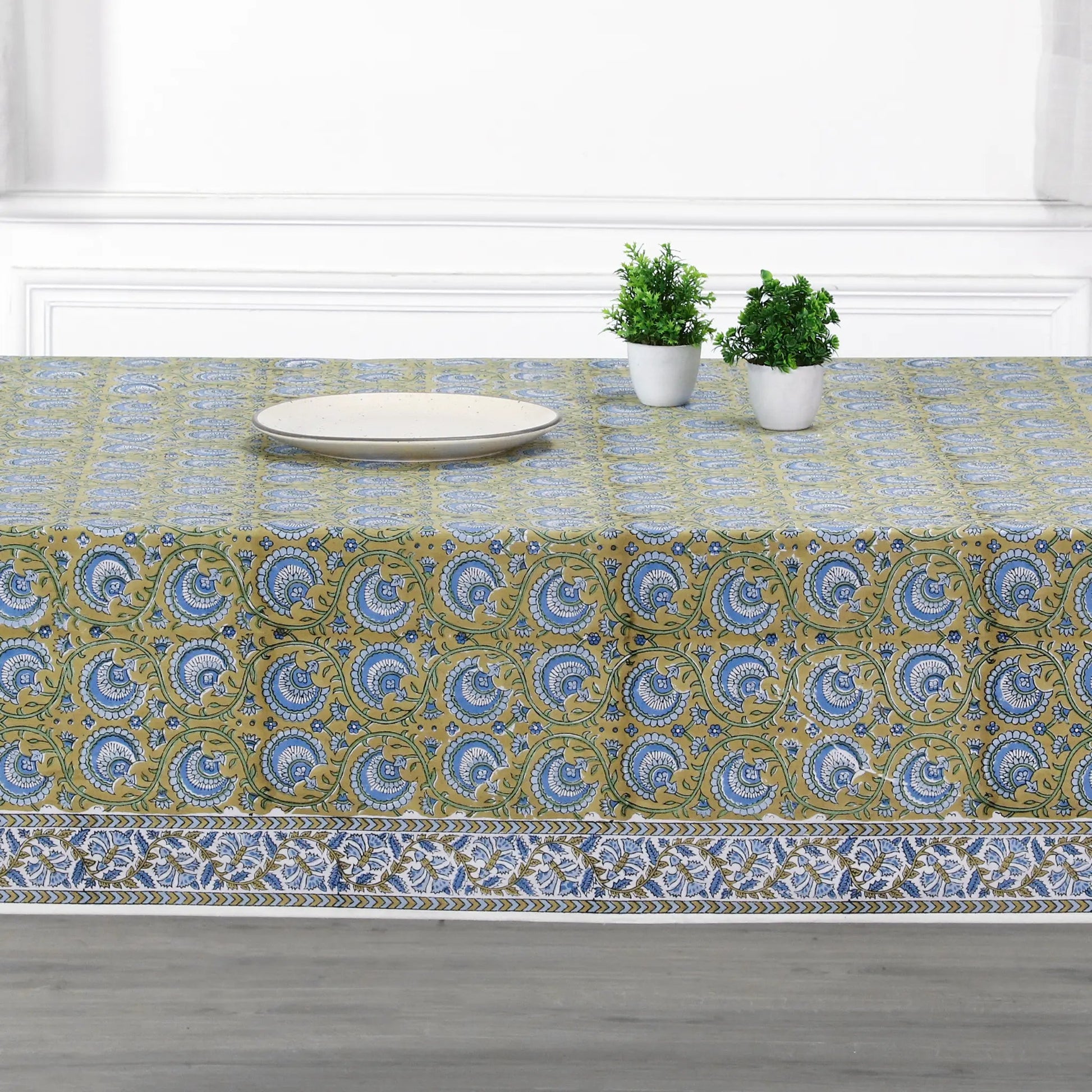 Tablecloth with a floral pattern on a dining table with plates and plants.