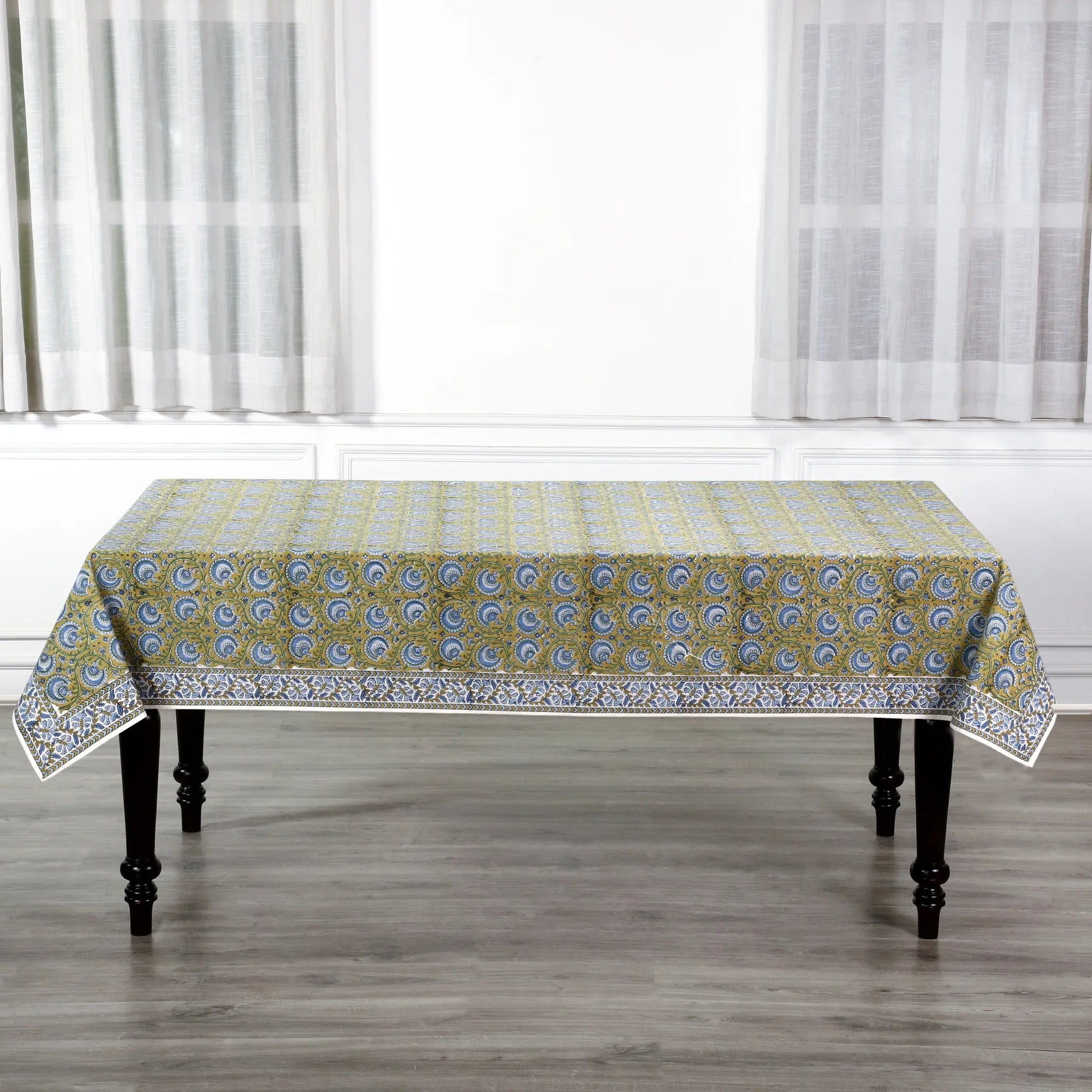 Patterned tablecloth on a wooden table with white curtains in the background