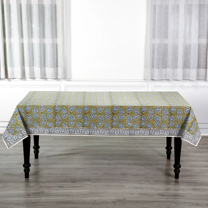 Patterned tablecloth on a wooden table with white curtains in the background