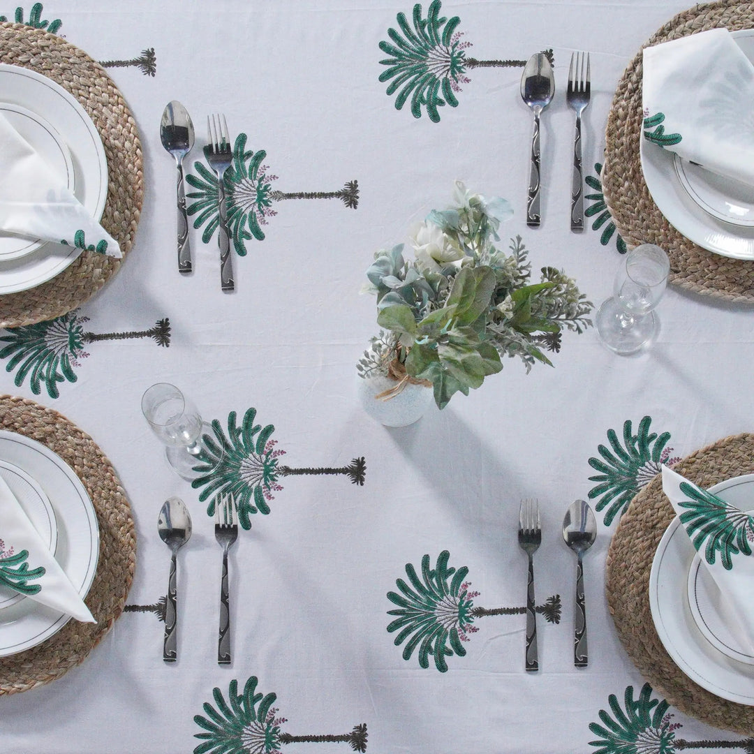 Table setting with white plates, silverware, and decorative tablecloth with palm tree pattern.