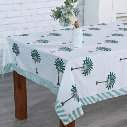Tablecloth with palm tree design on a wooden table against a white brick wall.