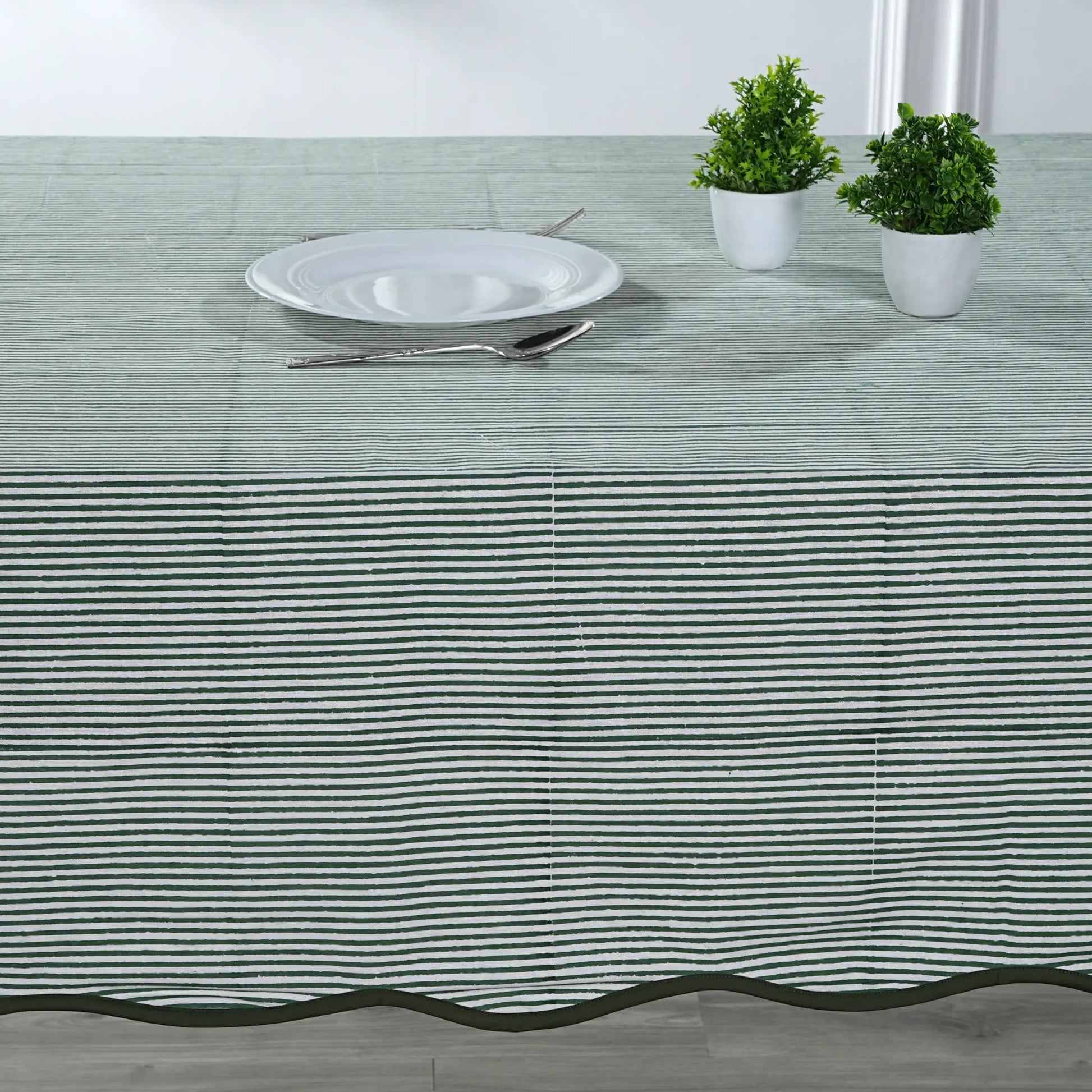 Tablecloth with black stripes on a table setting with a plate, cutlery, and plants.