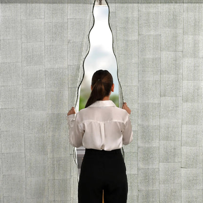 Person holding a large, wavy mirror against a textured wall.