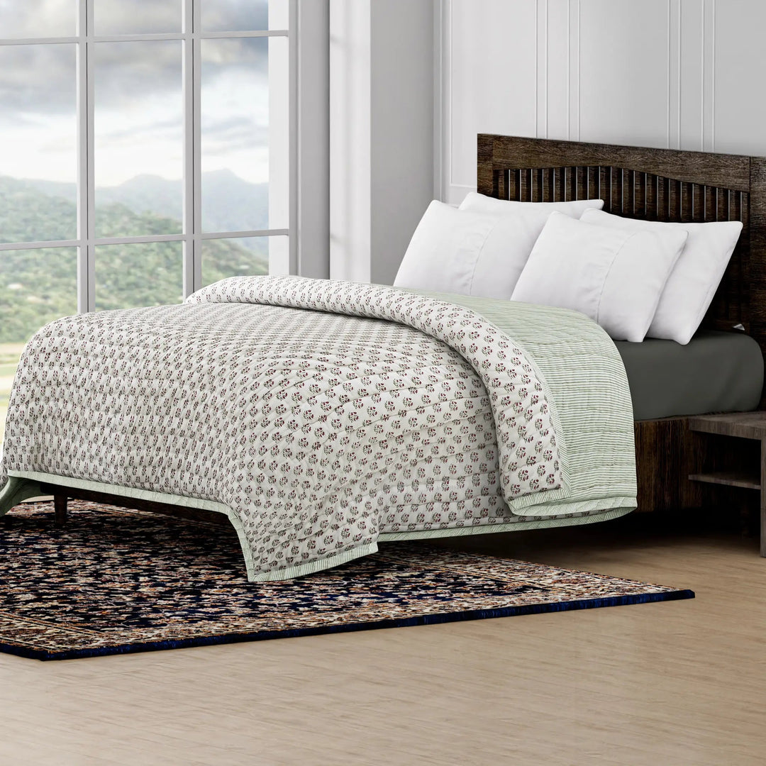 Bed with patterned quilt and white pillows in a room with large windows and a scenic view.