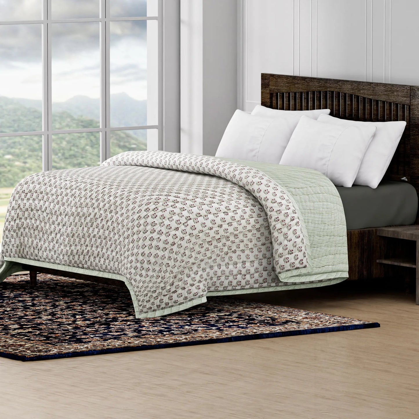 Bed with patterned quilt and white pillows in a room with large windows and a scenic view.