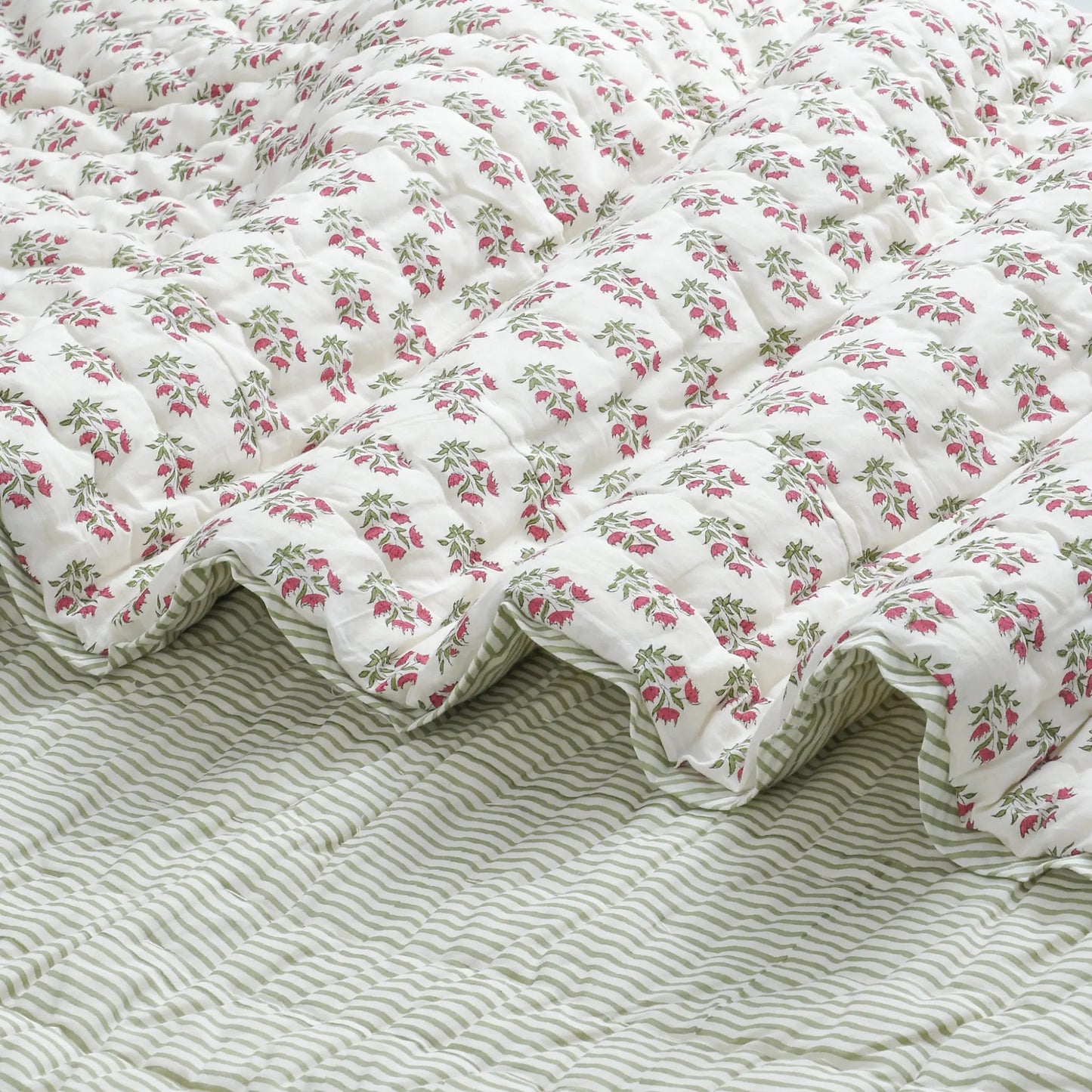 Floral quilt on a bed with a striped bedspread