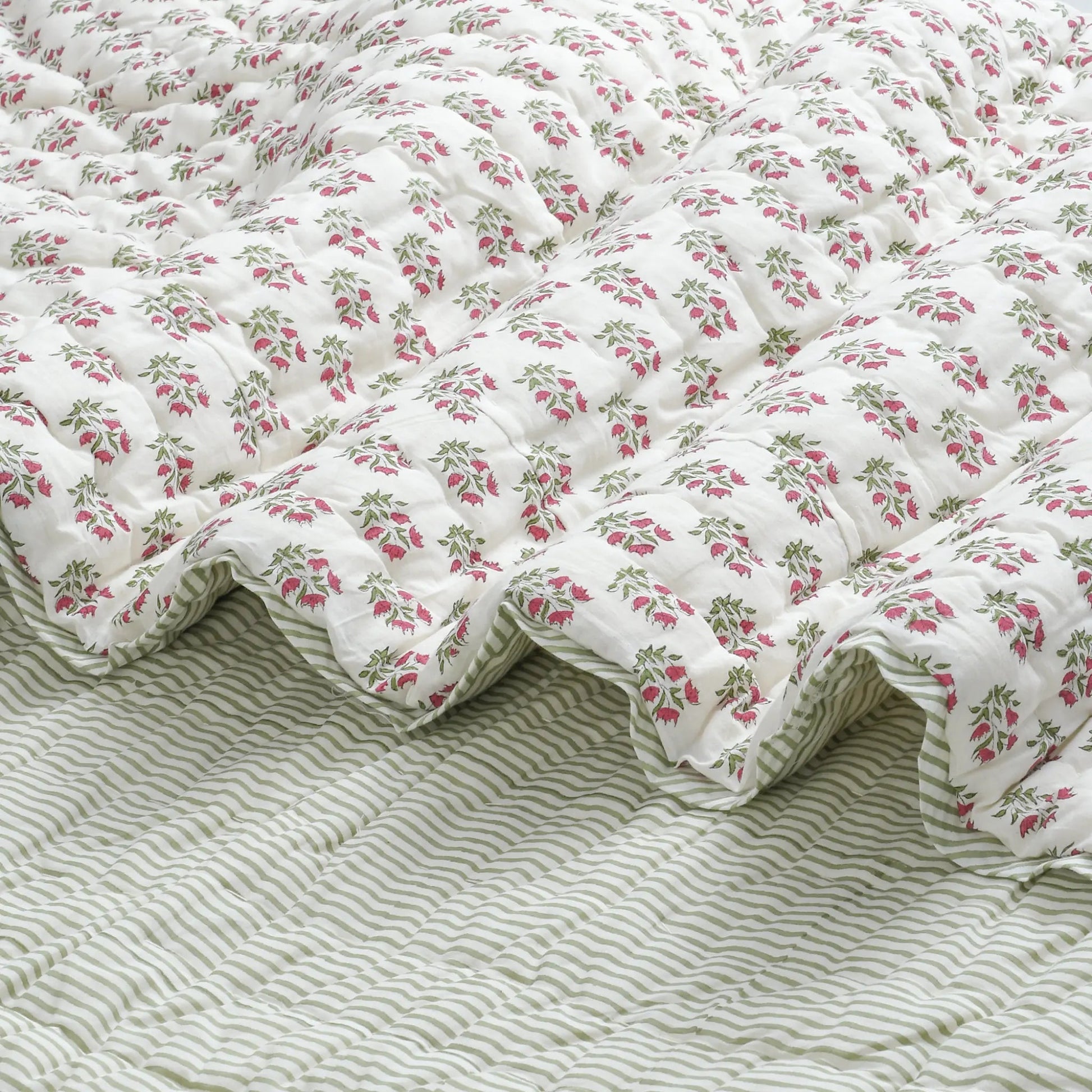 Floral quilt on a bed with a striped bedspread