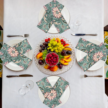 Table setting with floral napkins, fruit platter, and cutlery on a white tablecloth.