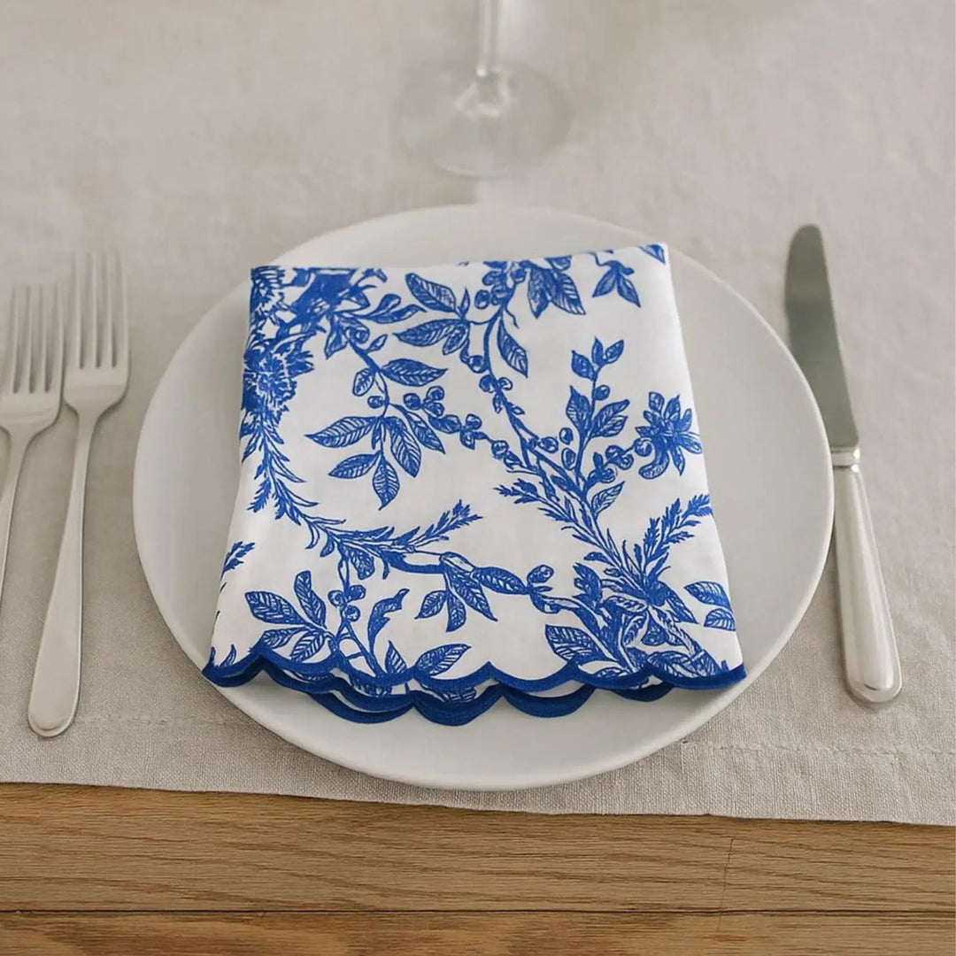Napkin with blue floral pattern on a white plate with cutlery on a beige tablecloth.