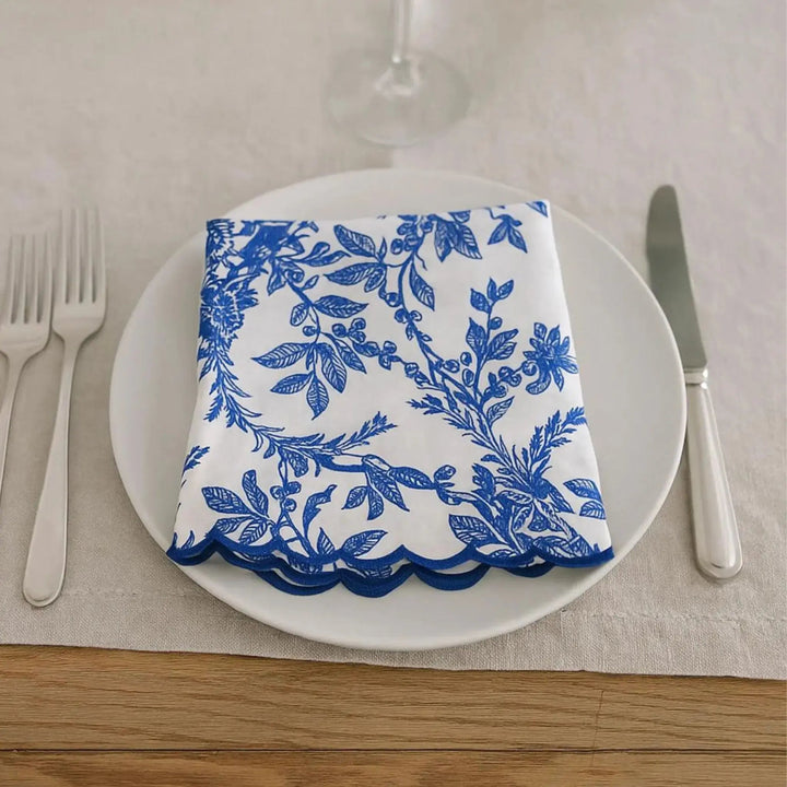 Napkin with blue floral pattern on a white plate with cutlery on a beige tablecloth.