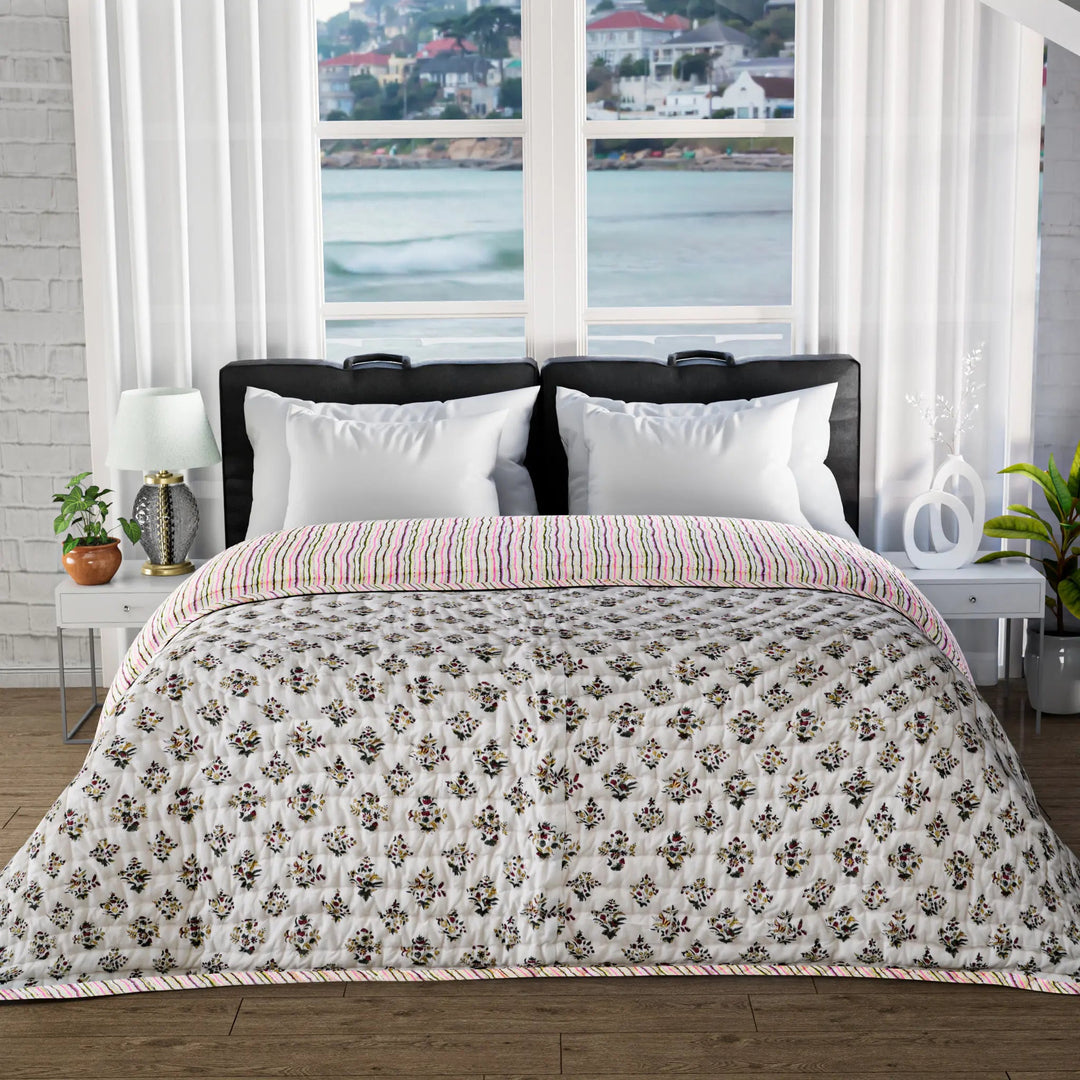 Bed with floral quilt and white pillows in a room with large windows showing a waterfront view.