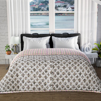 Bed with floral quilt and white pillows in a room with large windows showing a waterfront view.