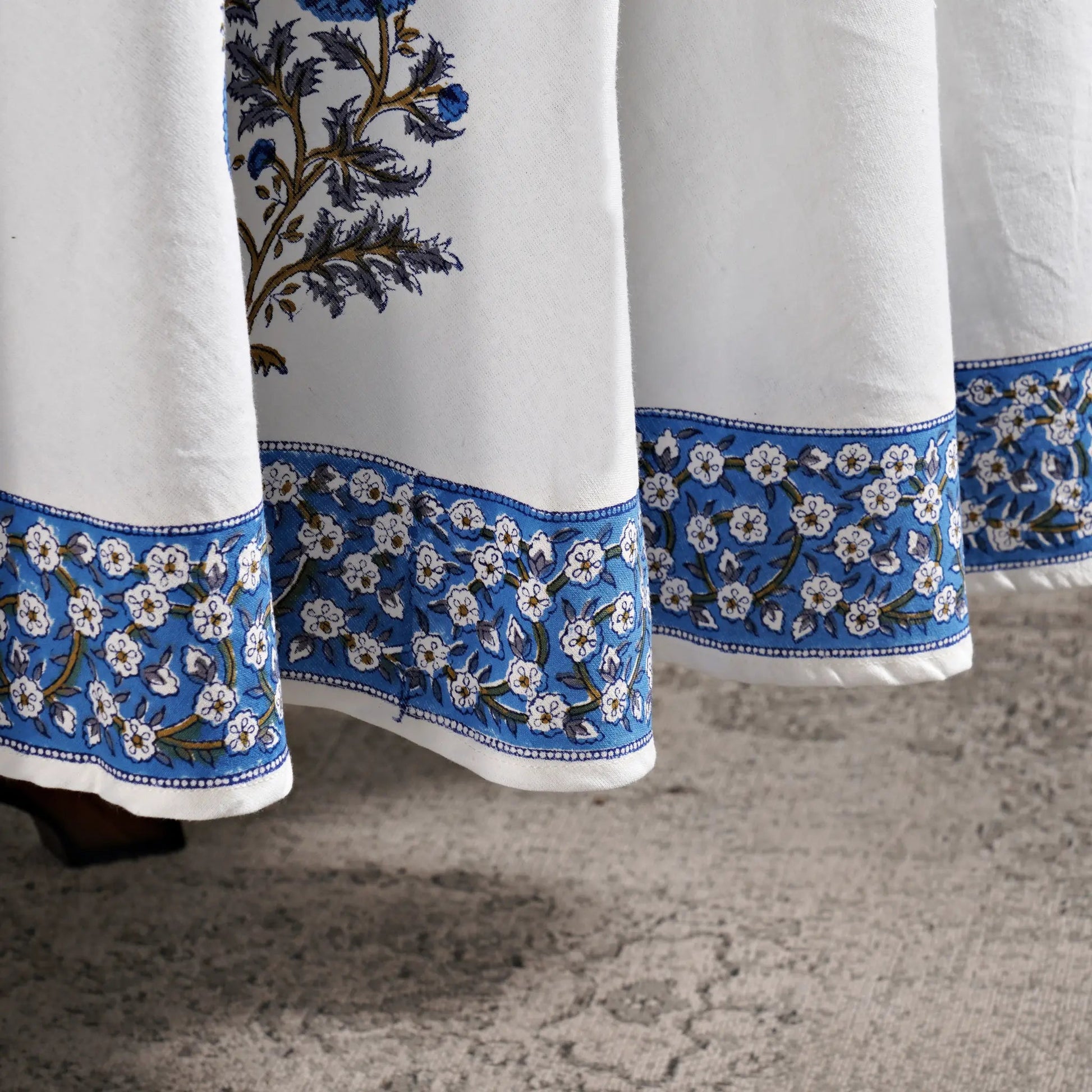 White curtains with blue floral embroidery on a textured floor.