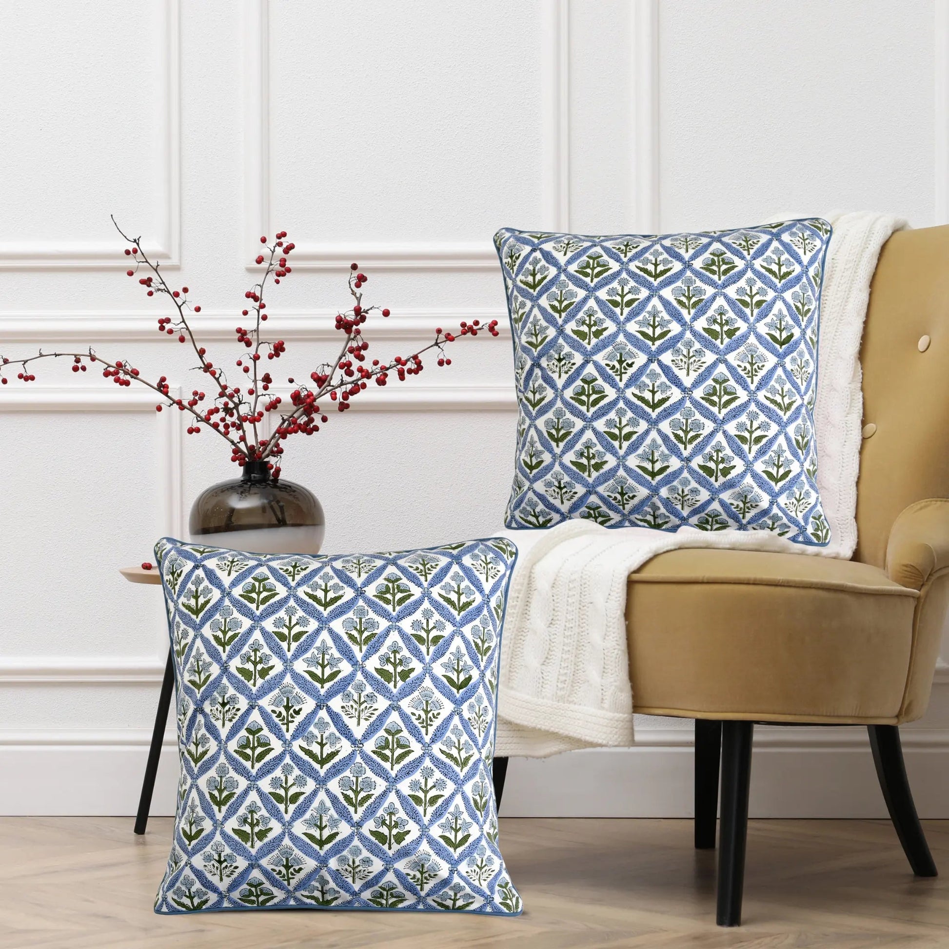 Two patterned pillows on a chair with a vase of red berries in the background.