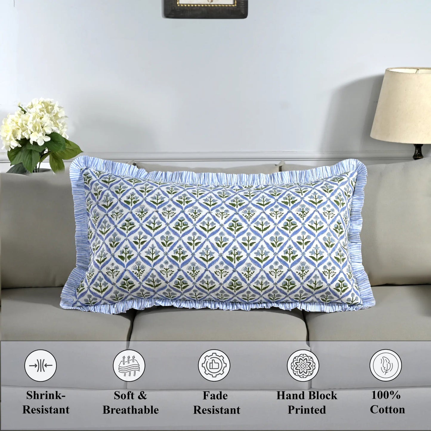 Cotton block print pillow cover placed on a bed with lamp and flowers in background.
