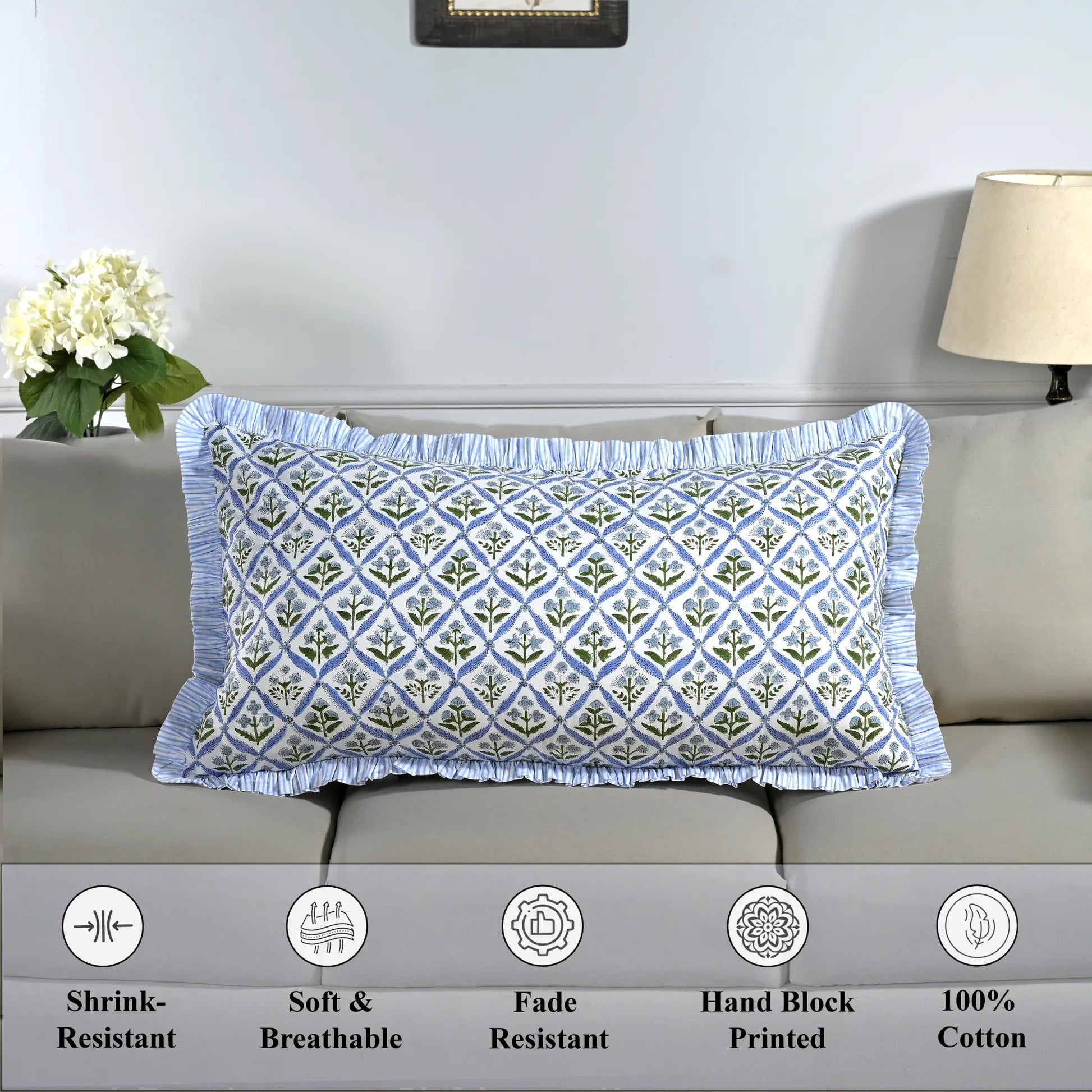 Cotton block print pillow cover placed on a bed with lamp and flowers in background.
