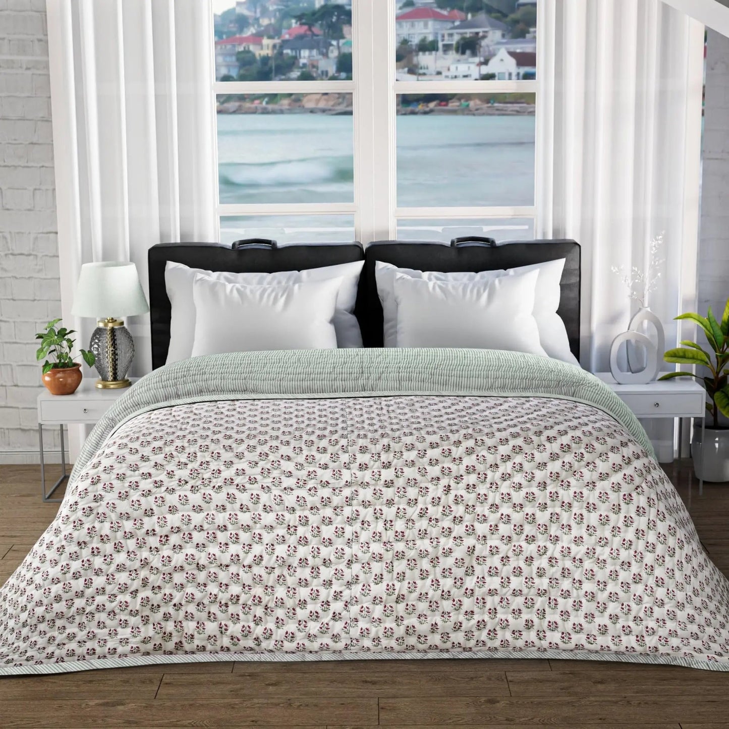 Bed with floral-patterned comforter in a room with large windows showing a waterfront view.