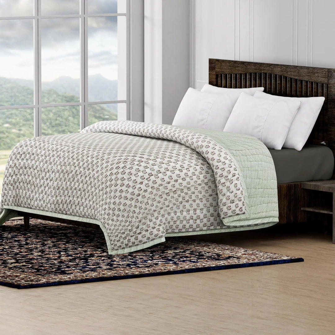 Bed with patterned quilt and white pillows in a room with large windows and a scenic view.