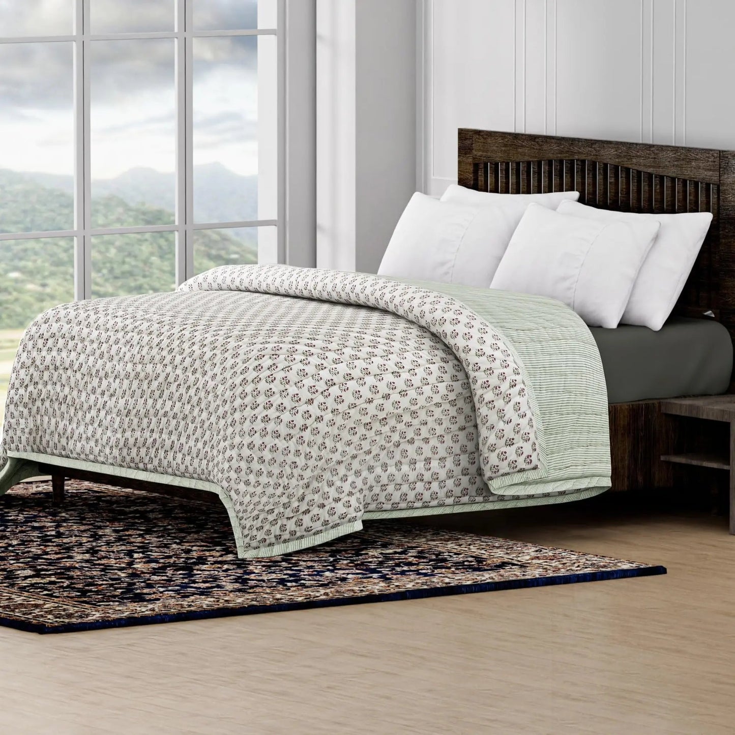 Bed with patterned quilt and white pillows in a room with large windows and a scenic view.