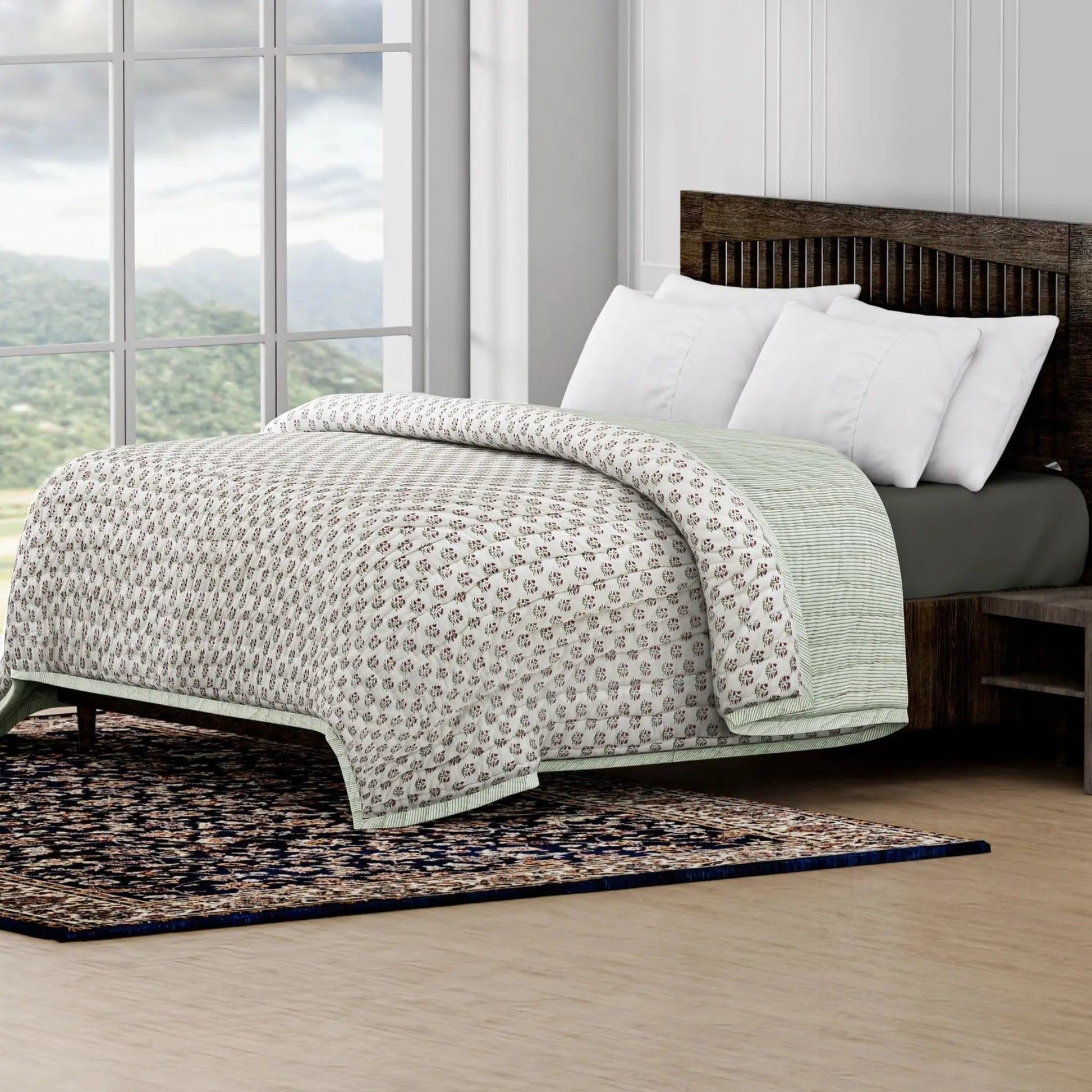 Bed with patterned quilt and white pillows in a room with large windows and a scenic view.