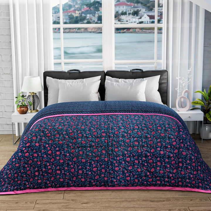 Bed with floral quilt and pillows in a room with large windows showing a view of water and buildings.