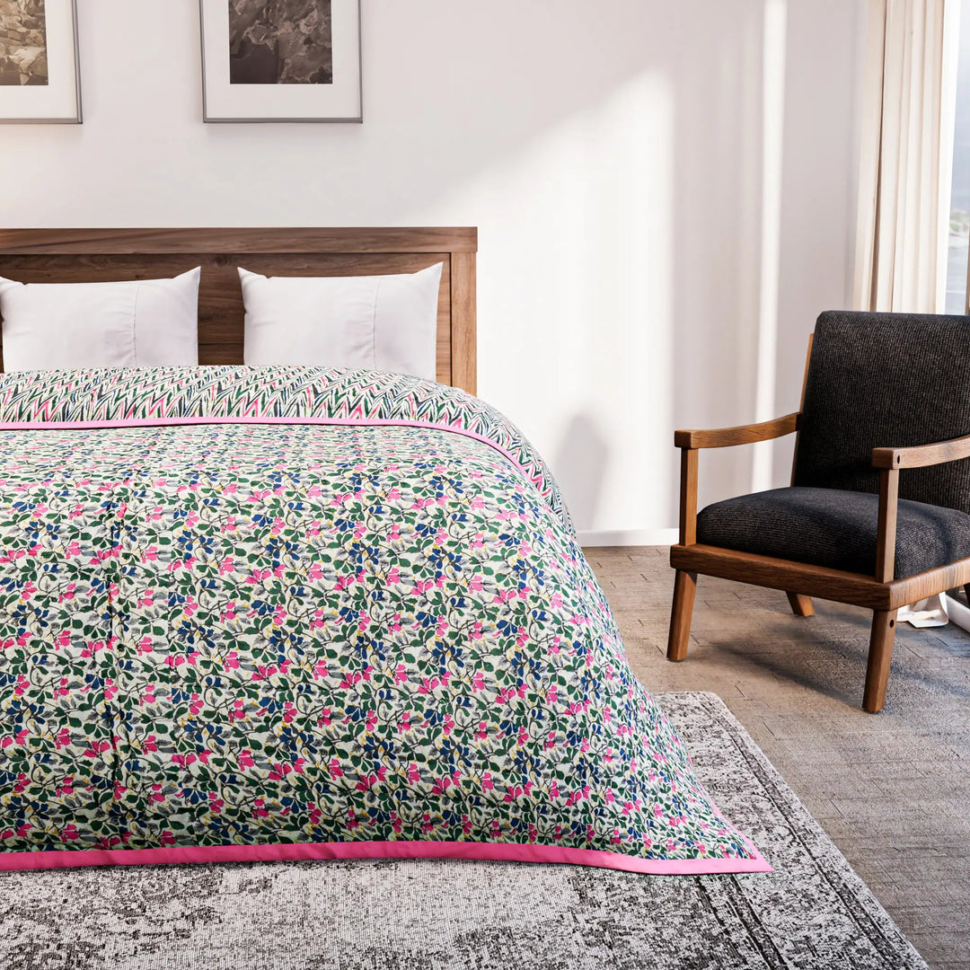 Bed with floral quilt in a bedroom setting with a chair and artwork on the wall.