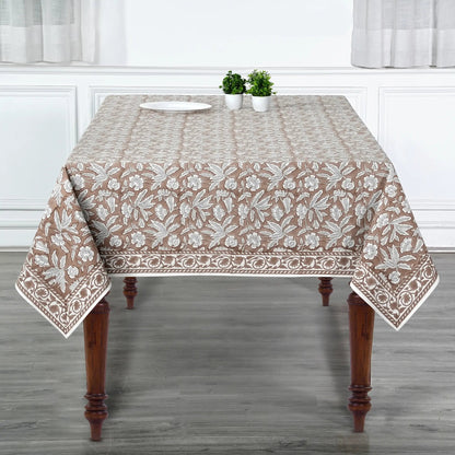Tablecloth with floral pattern on a wooden table in a room with white walls and gray floor.