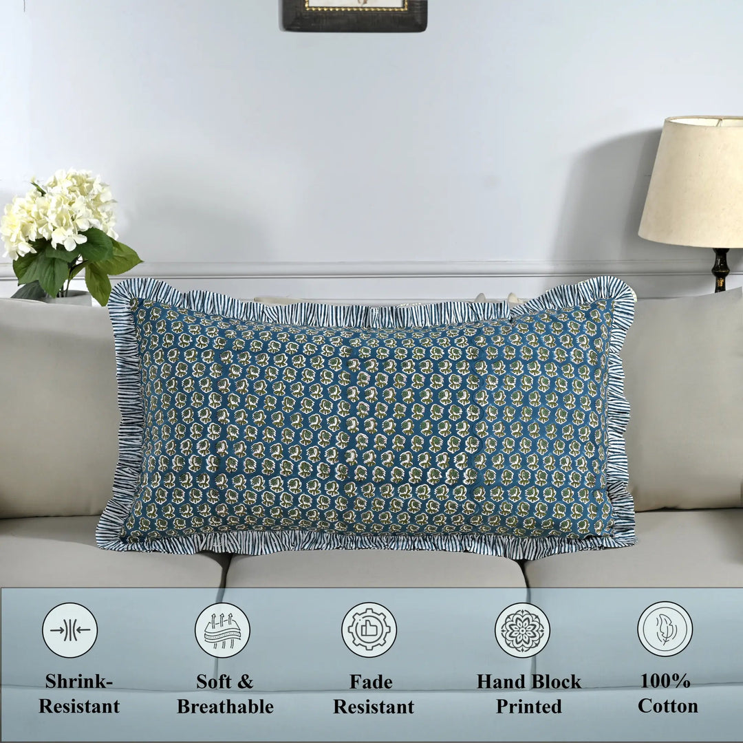 Cotton block print pillow cover placed on a bed with lamp and flowers in background.