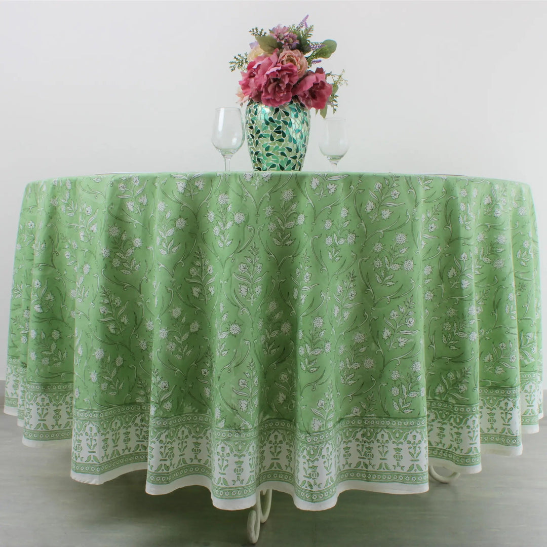 Green patterned tablecloth on a table with a vase of flowers and wine glasses.