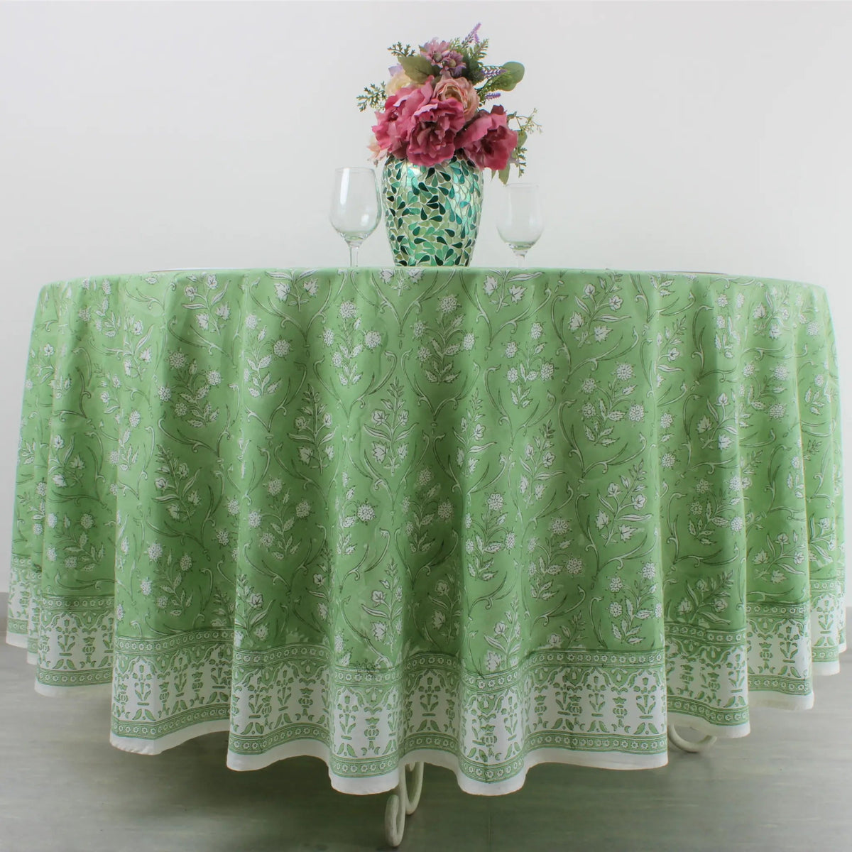 Green patterned tablecloth on a table with a vase of flowers and wine glasses.