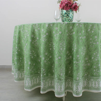 Green patterned tablecloth on a round table with a vase of flowers.