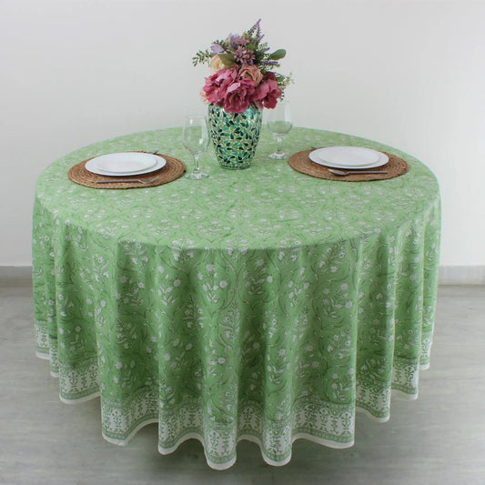 Round table with green floral tablecloth, plates, glasses, and a vase of flowers.