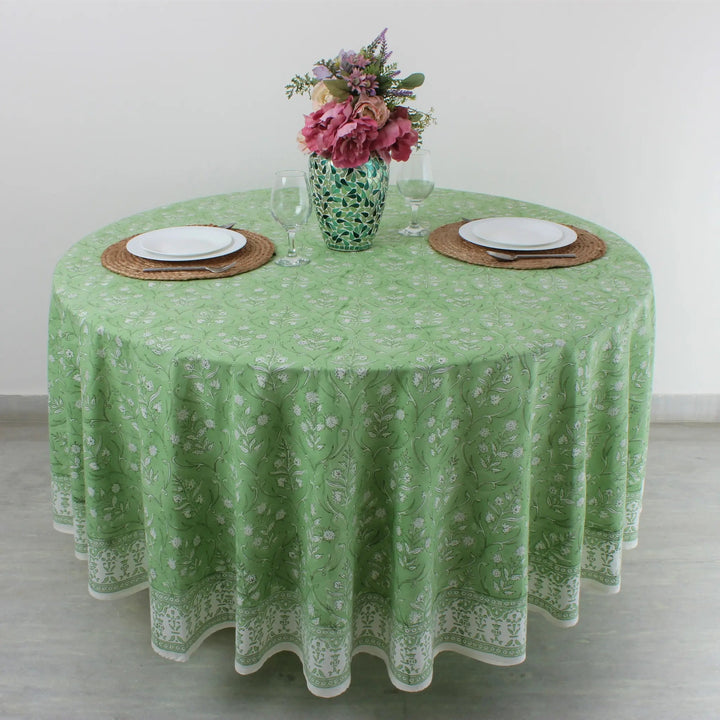 Round table with green floral tablecloth, plates, glasses, and a vase of flowers.