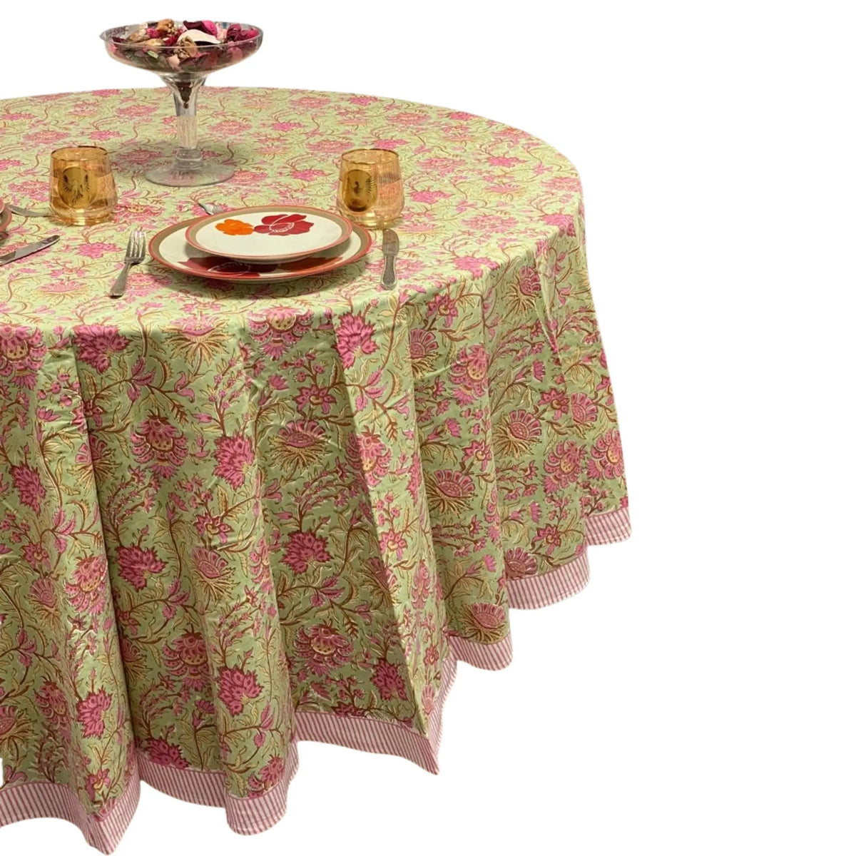 Round table with a floral tablecloth, plates, and glasses on a white background