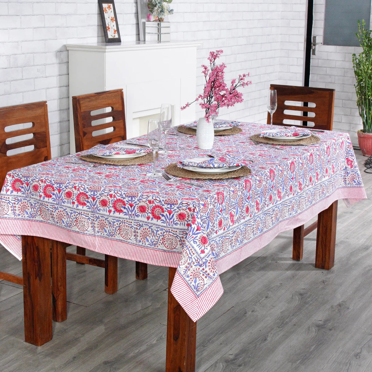 Dining table with a floral tablecloth, wooden chairs, and decorative items.