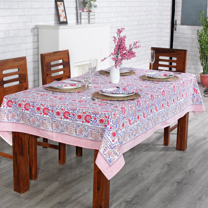 Dining table with a floral tablecloth, wooden chairs, and decorative items.