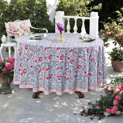 Floral patterned tablecloth on a table outdoors with chairs and flowers.