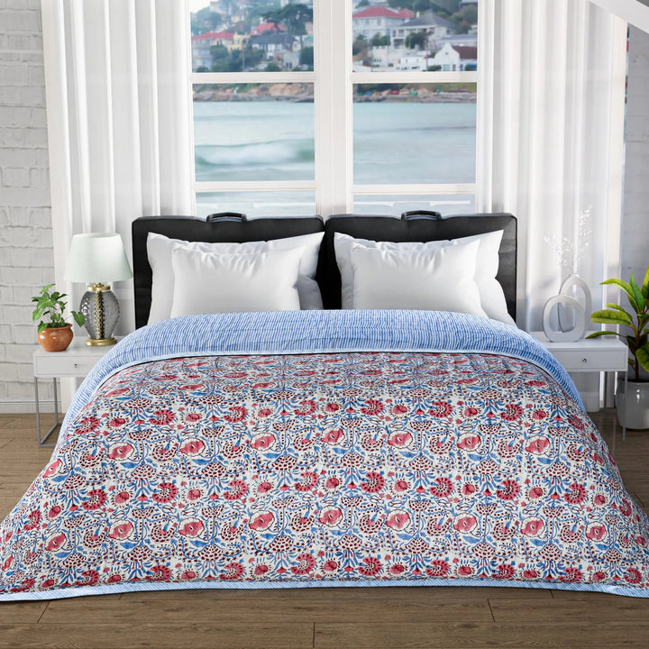 Floral patterned comforter on a bed with a window view of water and buildings.