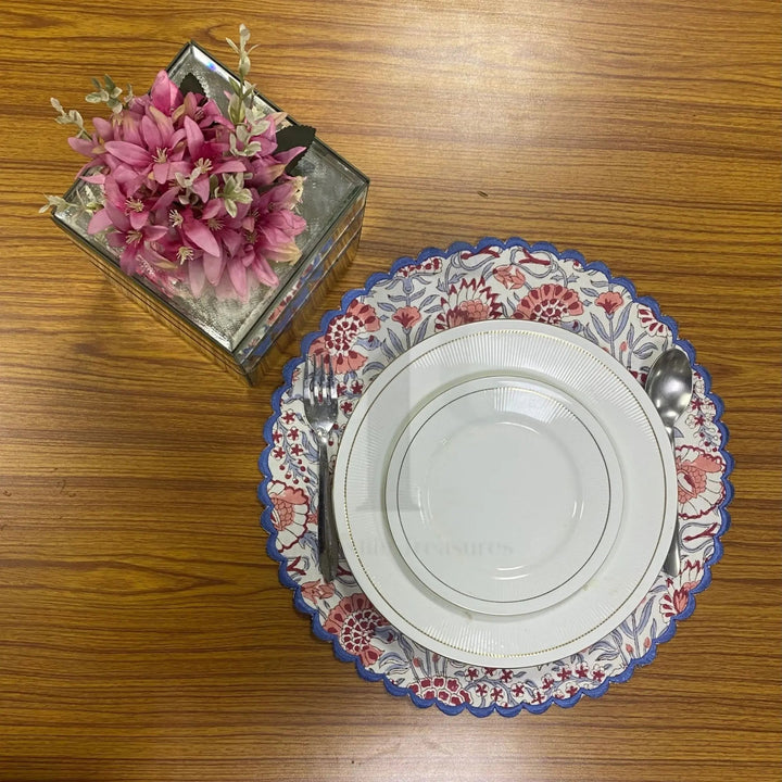 Decorative plate with floral rim on a wooden table, next to a small box of pink flowers.