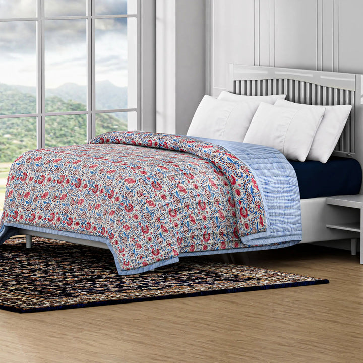 Floral quilt on a bed in a room with large windows and a view of greenery outside.
