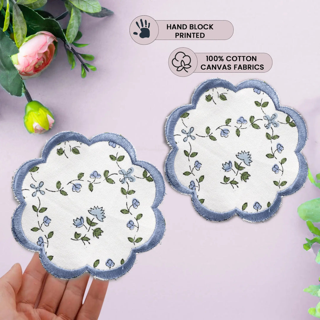 Two floral coasters with scalloped edges on a light pink background, held by a hand.