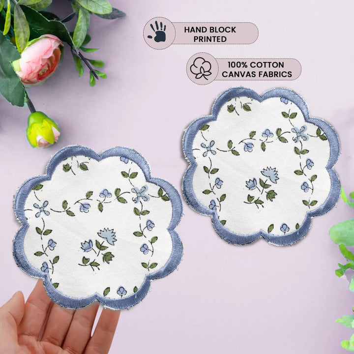 Two floral coasters with scalloped edges on a light pink background, held by a hand.