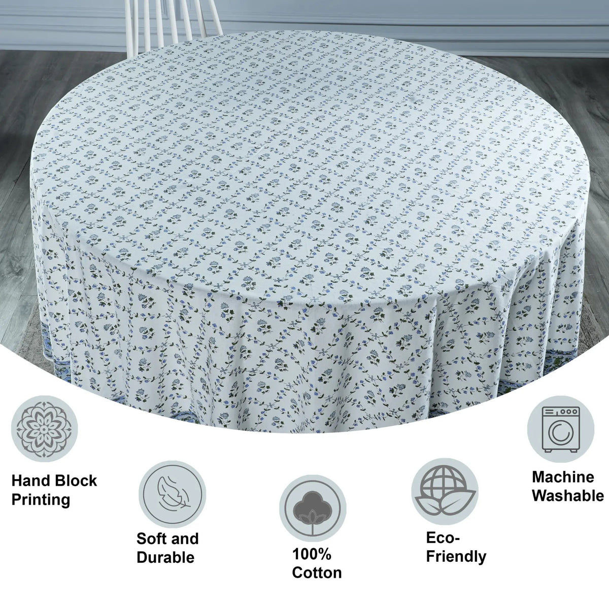 Round table covered with a floral patterned tablecloth on a wooden floor.