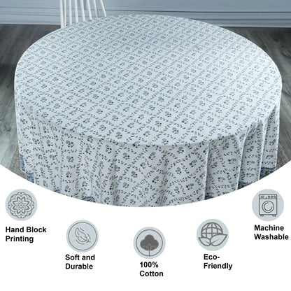 Round table covered with a floral patterned tablecloth on a wooden floor.