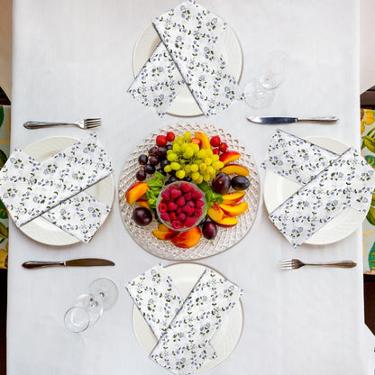 Table setting with floral plates, fruit platter, and cutlery on a white tablecloth.