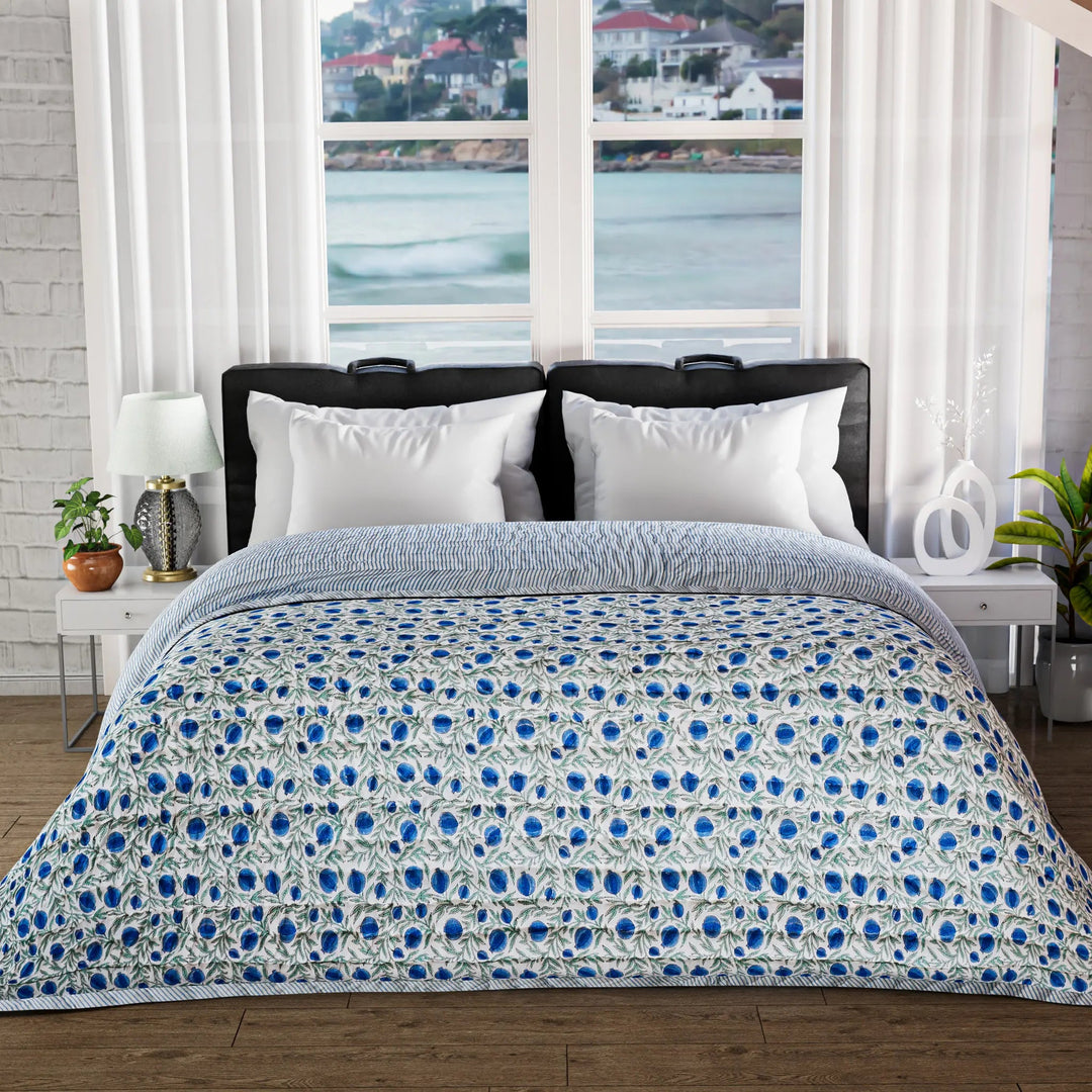 Bed with blue and white patterned comforter in a room with large windows showing a waterfront view.