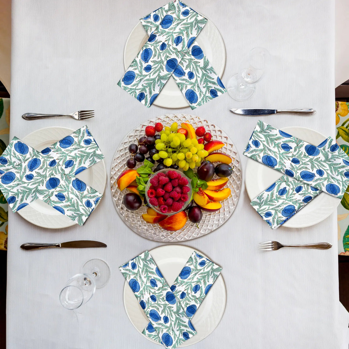 Table setting with floral-patterned plates and napkins, featuring a fruit platter in the center.