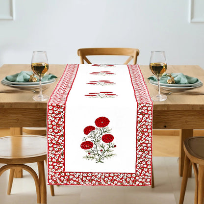 Dining table set with a red and white floral table runner, glasses, and plates.